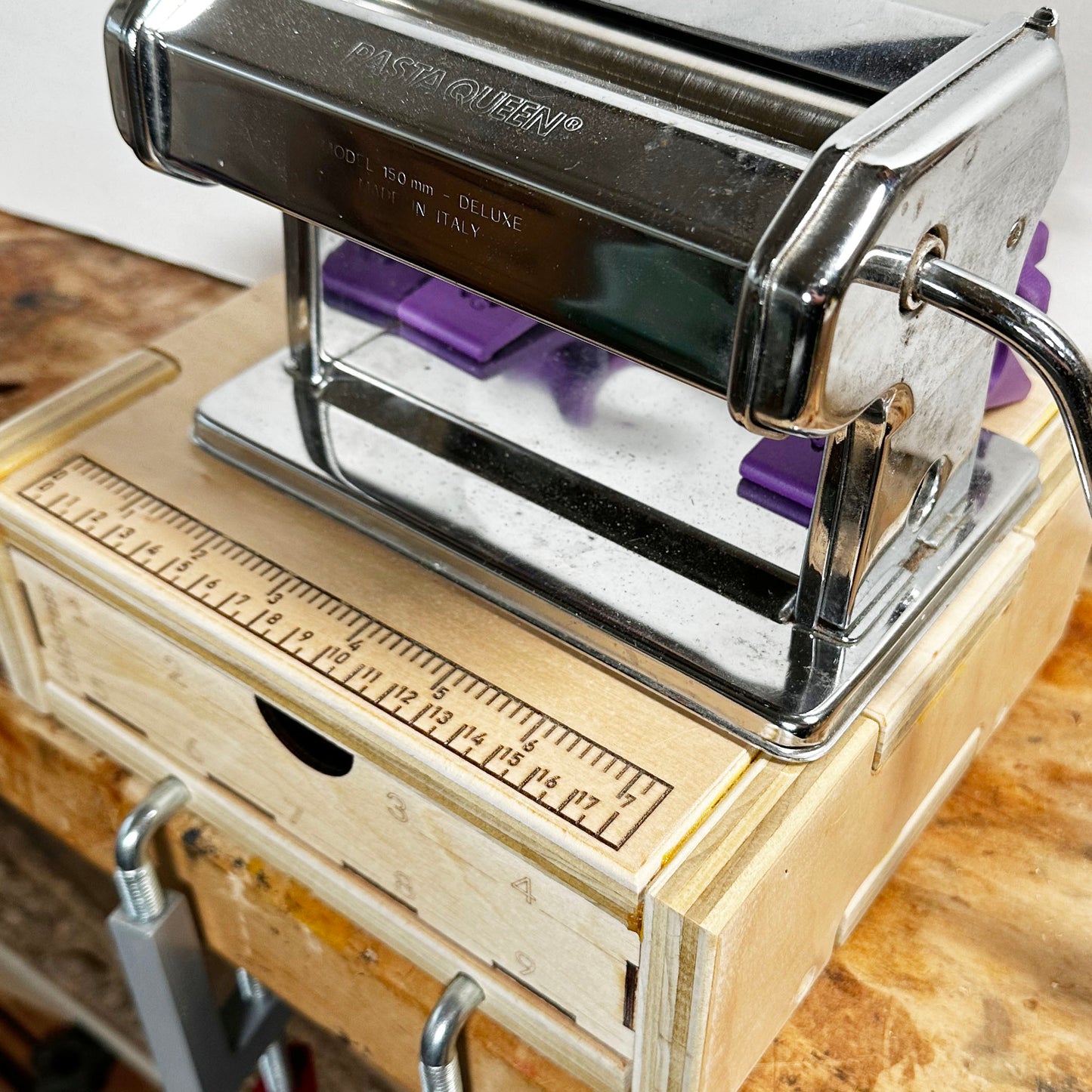 A close-up of the pasta machine base showing a pasta machine clamped on the base and the base clamped to a workbench.