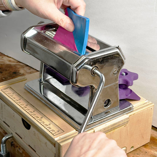 A pasta machine about to crank polymer clay through the rollers.